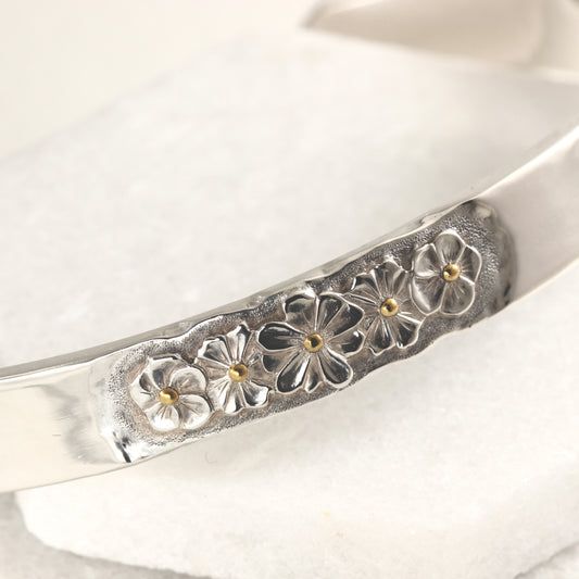 Close up of hand-formed sterling silver cuff with 24k gold accents and engraved texture