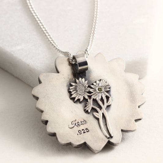 Back side of Wild Radiance Daisy Pendant with gold center in sterling silver on white marble background, showing engraved daisy with Montana sapphire