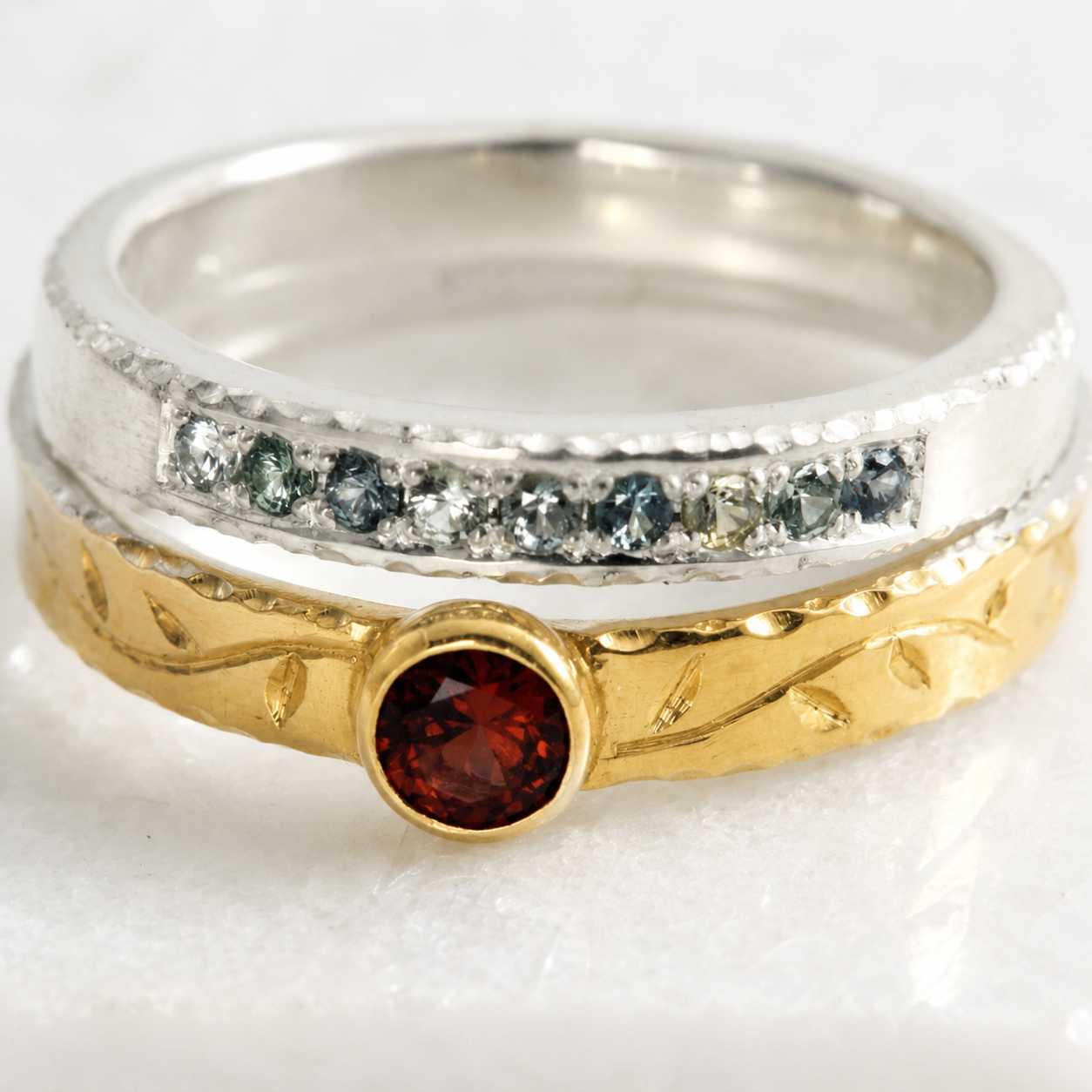 Close up of sterling silver Coastal Stacking Ring with small Montana sapphires and 14K gold Tendril Stacking Ring with Malaya Garnet