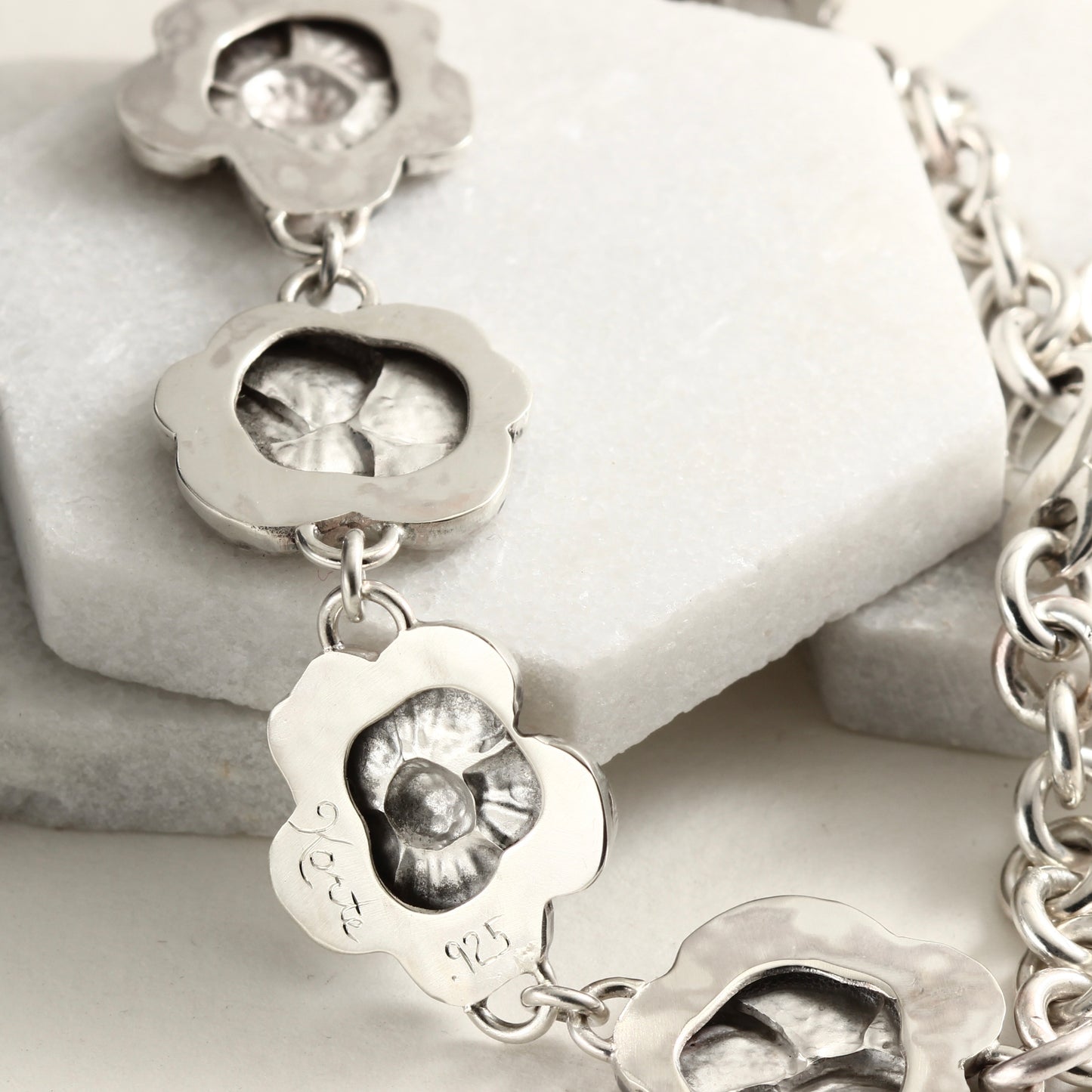 Back side of hand-formed sterling silver bracelet featuring linked floral elements, shaped using chasing and repoussé. A sculptural, articulated piece inspired by natural bloom.