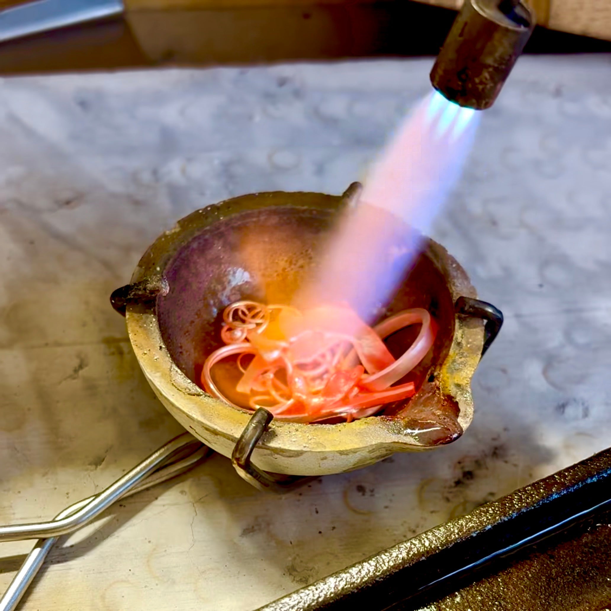 Using a torch to melt scrap metal to form an ingot to make a new piece of jewelry