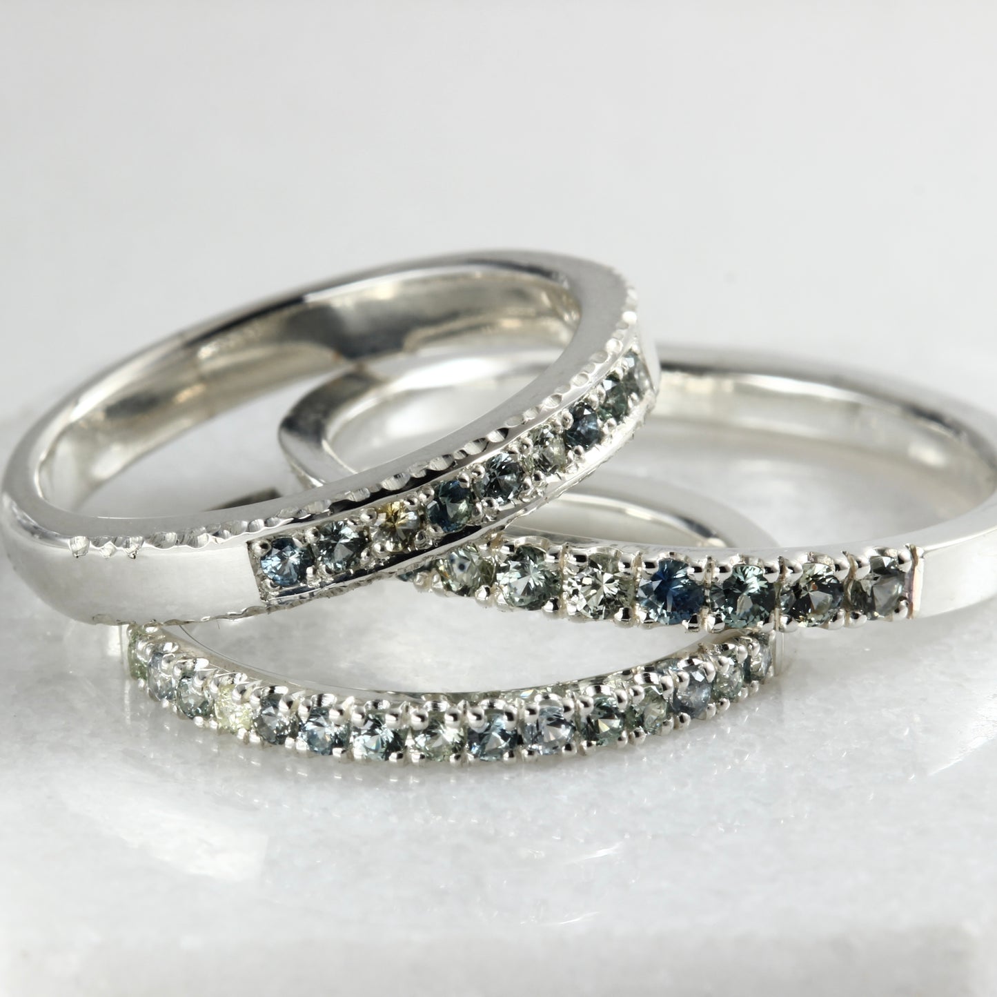 Three different sterling silver stacking rings set with Montana sapphires on a white marble surface.