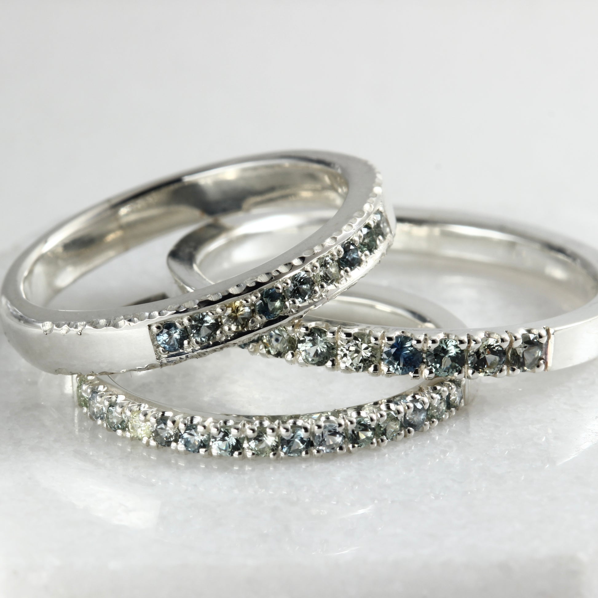 Three different sterling silver stacking rings set with Montana sapphires on a white marble surface.