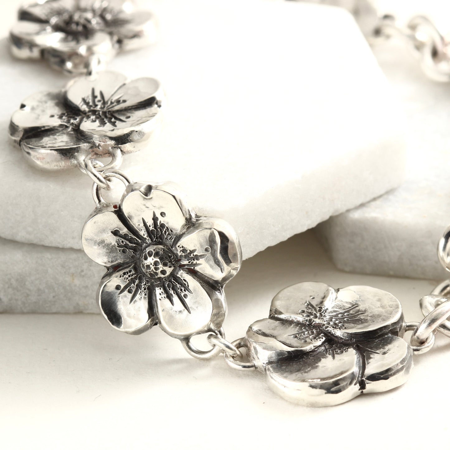 Hand-formed sterling silver bracelet featuring linked floral elements, shaped using chasing and repoussé. A sculptural, articulated piece inspired by natural bloom.