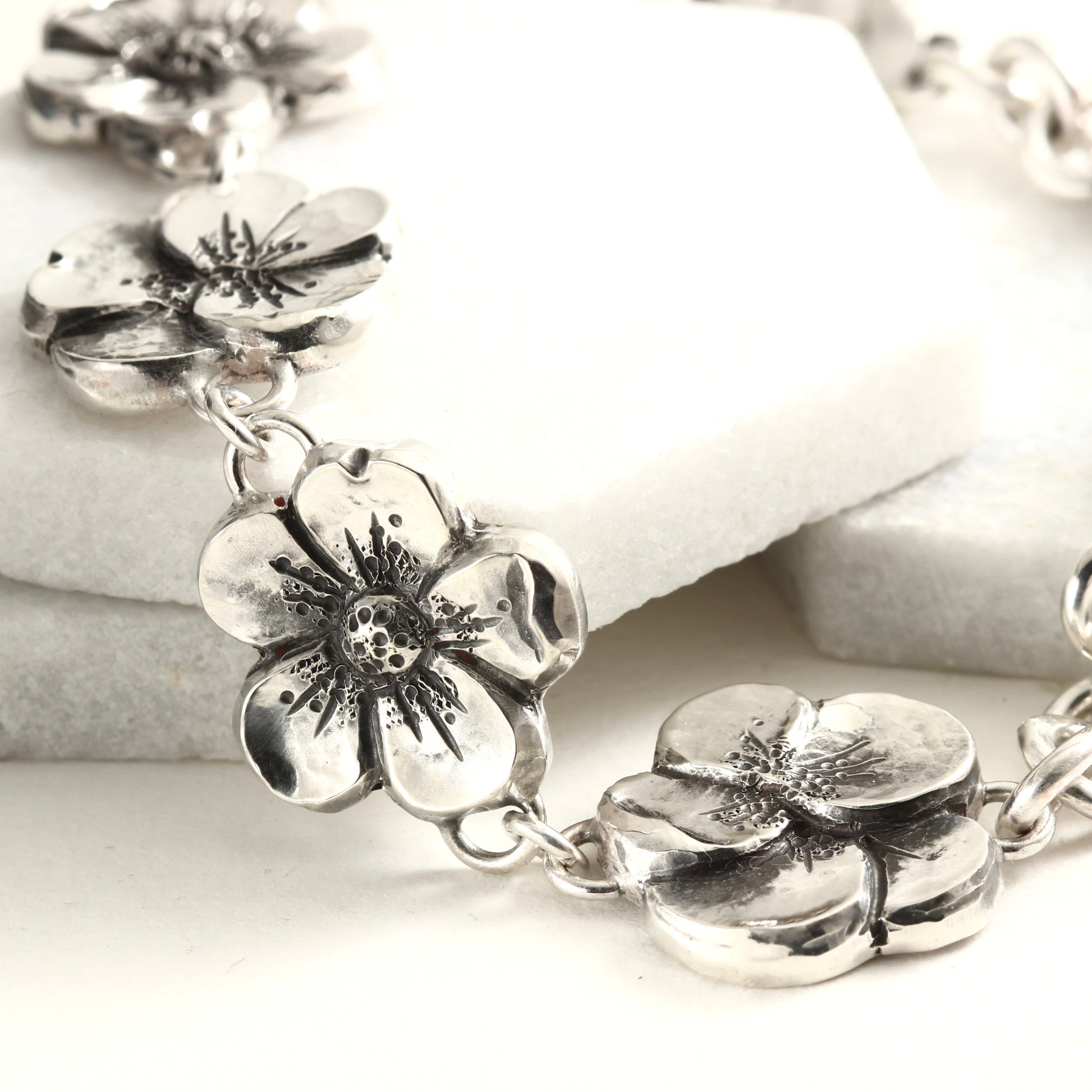 Hand-formed sterling silver bracelet featuring linked floral elements, shaped using chasing and repoussé. A sculptural, articulated piece inspired by natural bloom.