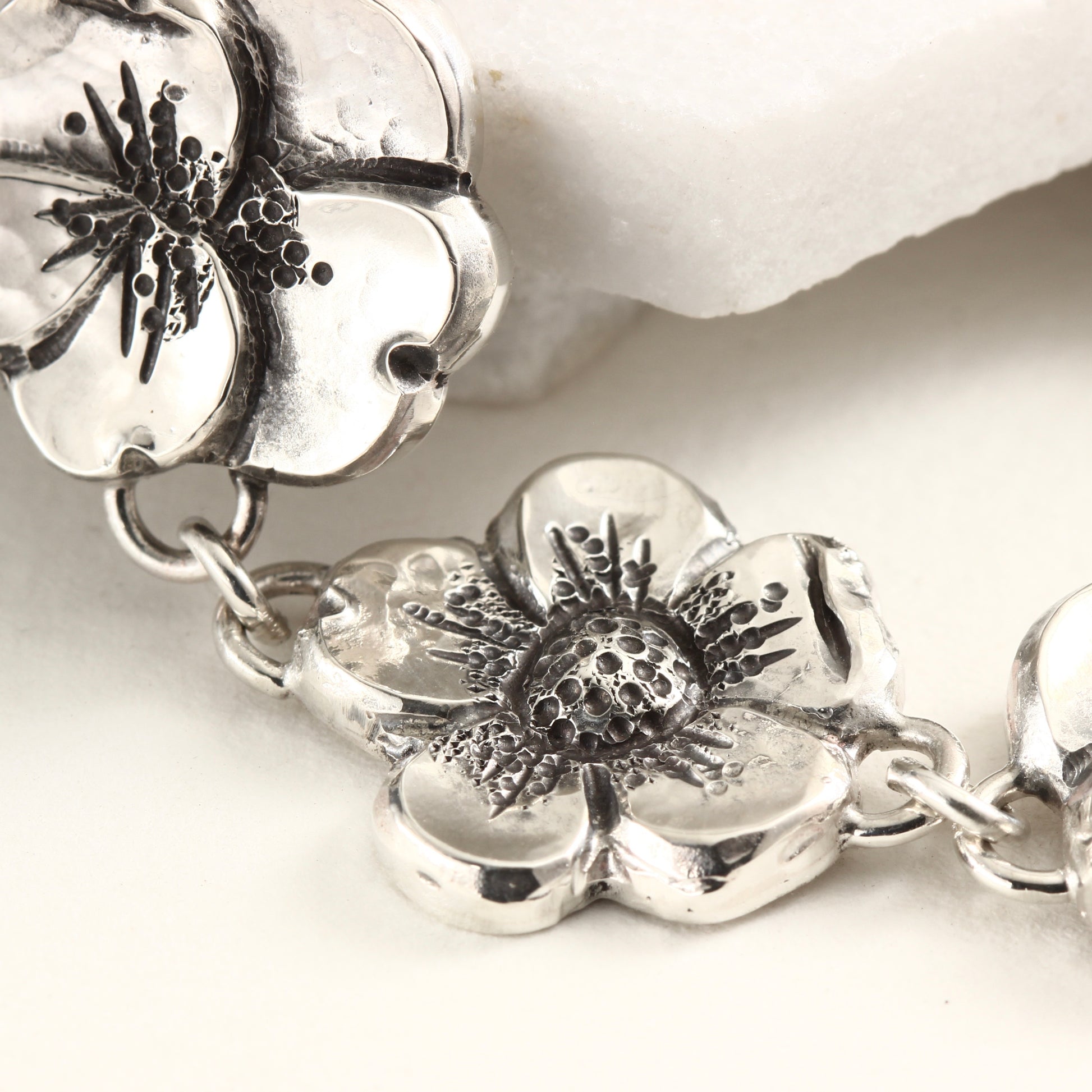 Close up of single bloom of hand-formed sterling silver bracelet featuring linked floral elements, shaped using chasing and repoussé. A sculptural, articulated piece inspired by natural bloom.