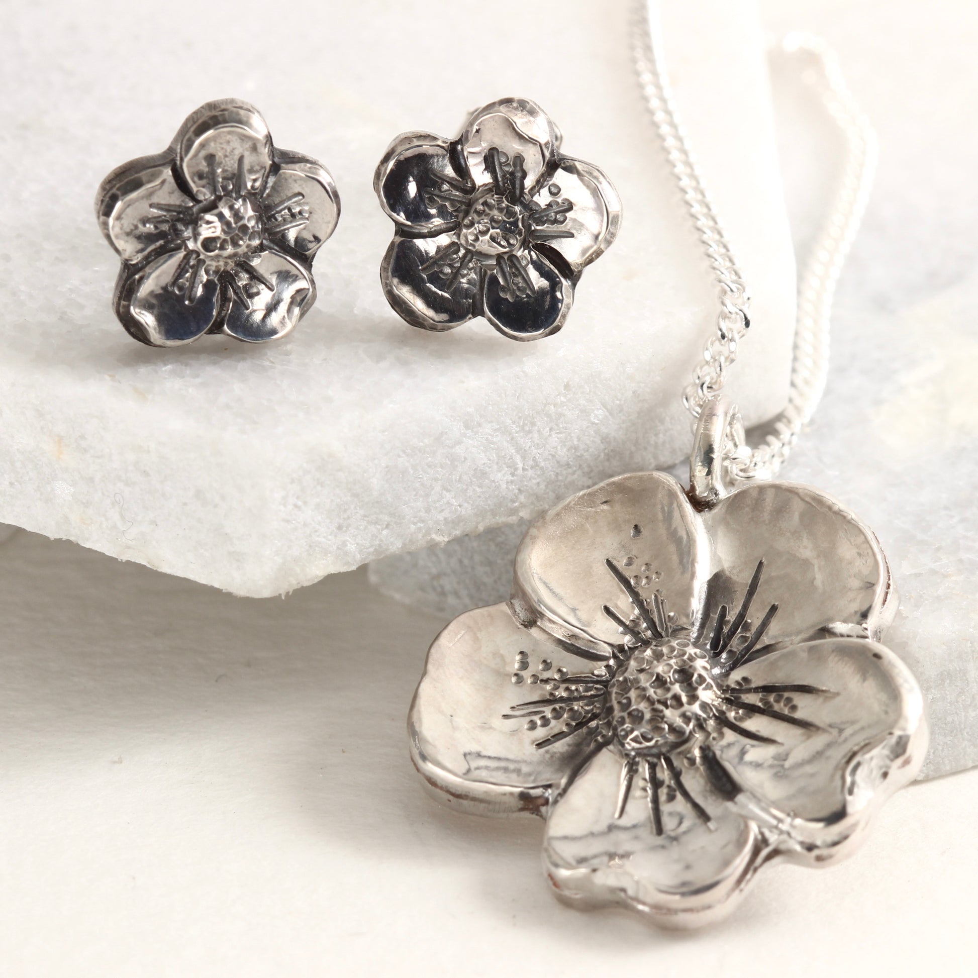 Styled shot of Wild Bloom Pendant and Wild Bloom Stud Earrings on white marble tile