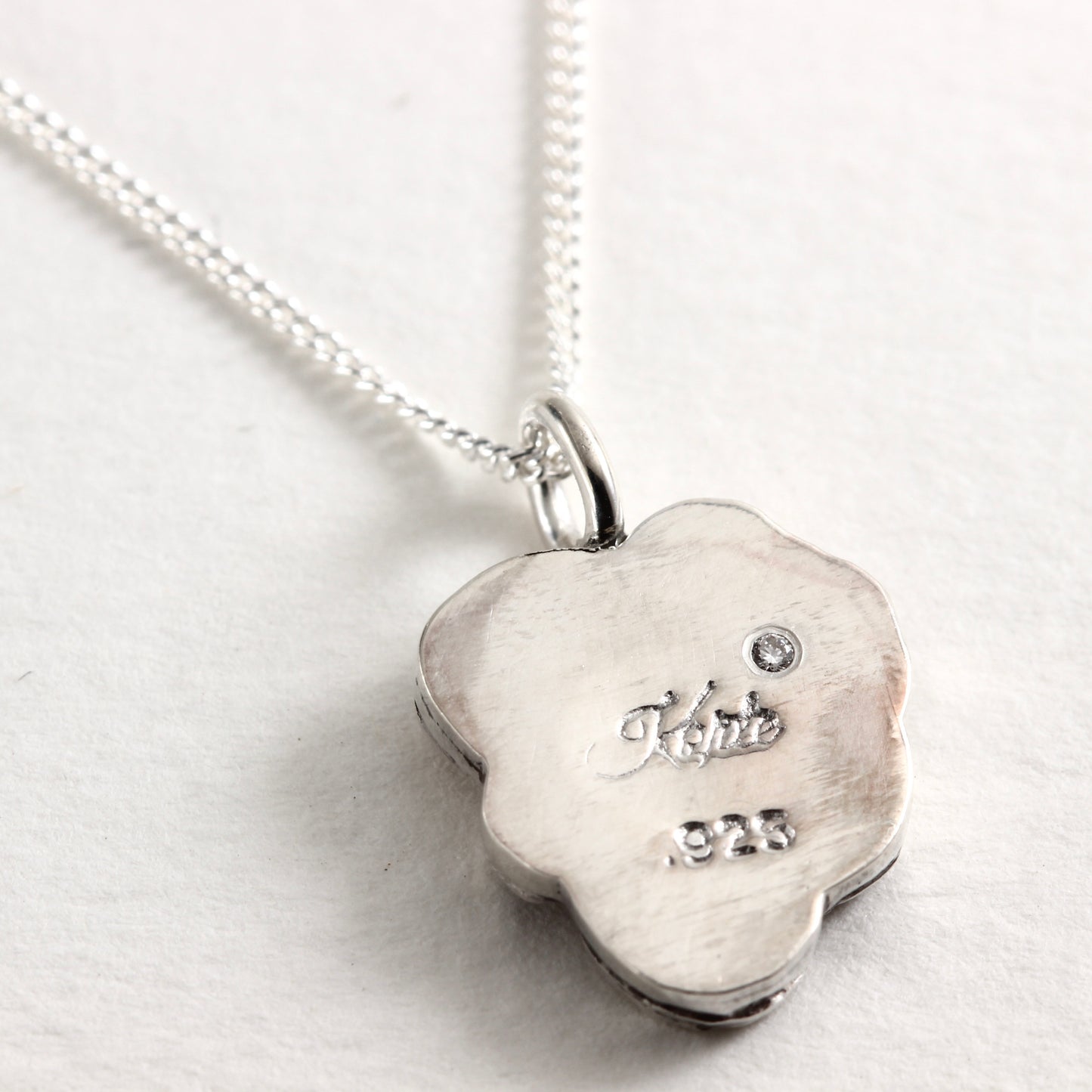 The back side of the Wild Bloom Violet Pendant in sterling silver, showing small diamond and maker’s mark