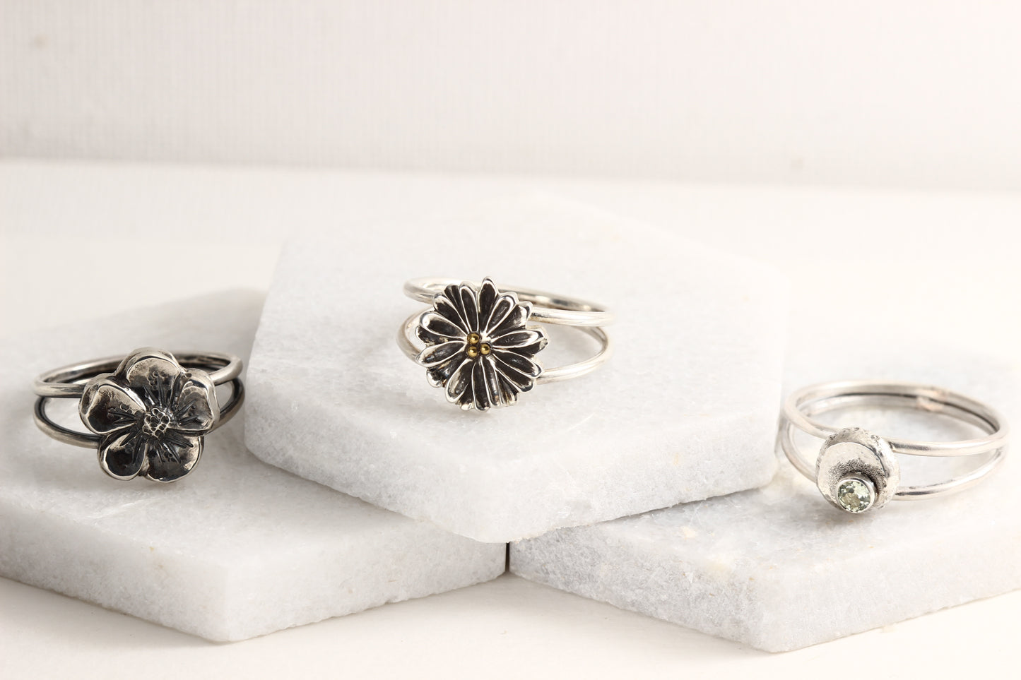 Several rings from the Wild Blooms collection in sterling silver, handcrafted flower rings, on a white marble background