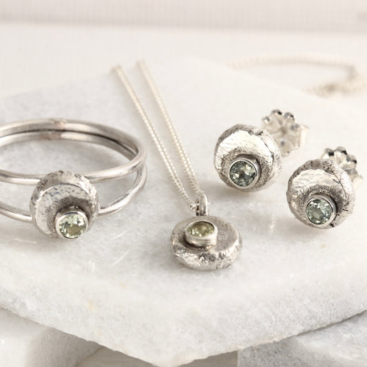 Pieces from the Wild Bud series with earrings, a pendant and a ring, all containing a Montana Sapphire and shown on a white marble background