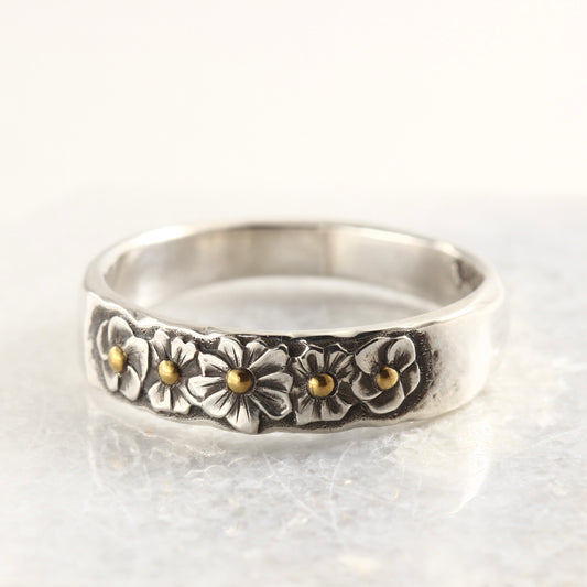 Wild Meadow Half Band in sterling silver with gold accents, a hand carved flower ring shown on a white marble tile