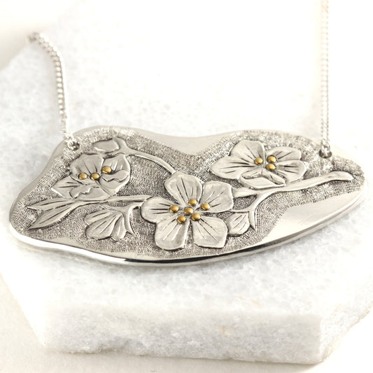 Wild Meadow Spring Branch Pendant in sterling silver with gold accents, a hand carved flower pendant shown on white marble tile