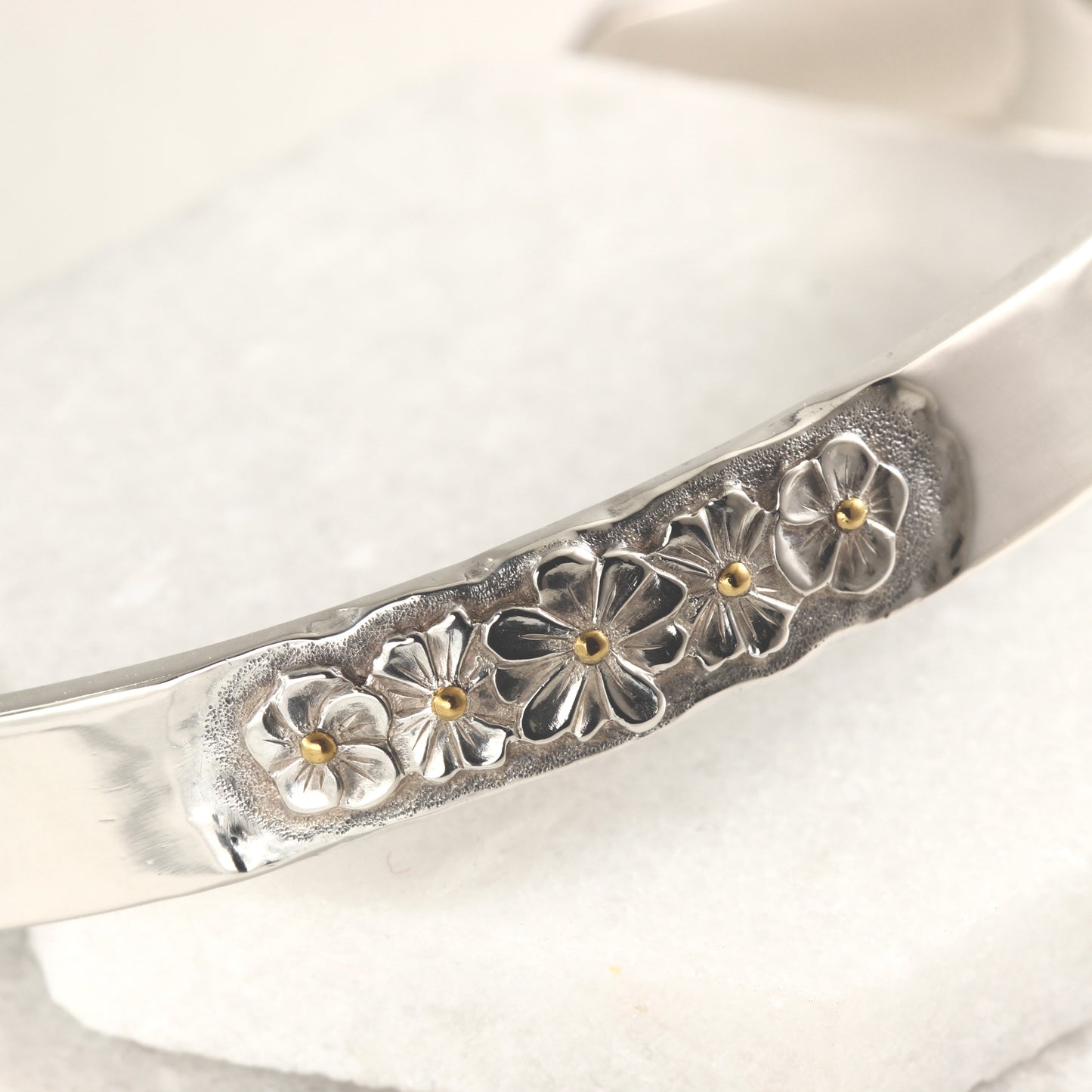 Close up of hand-formed sterling silver cuff with 24k gold accents and engraved texture
