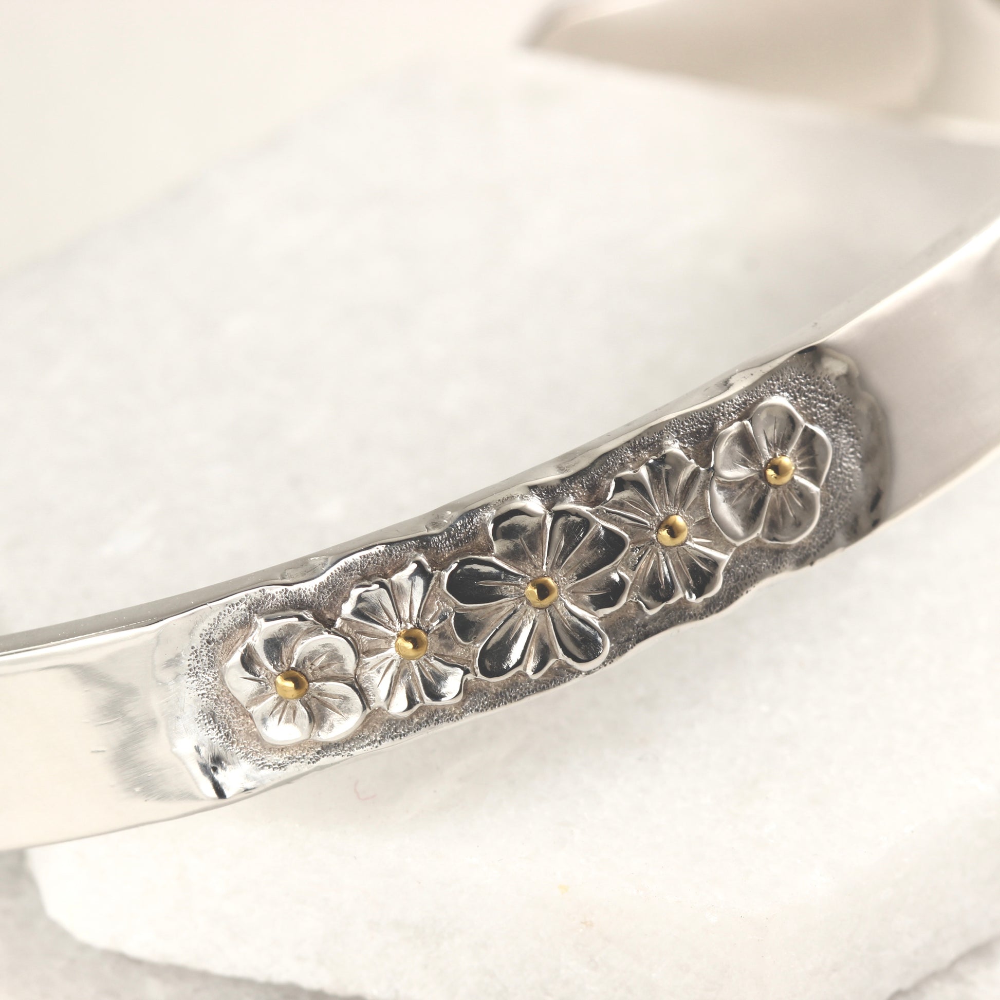 Close up of hand-formed sterling silver cuff with 24k gold accents and engraved texture