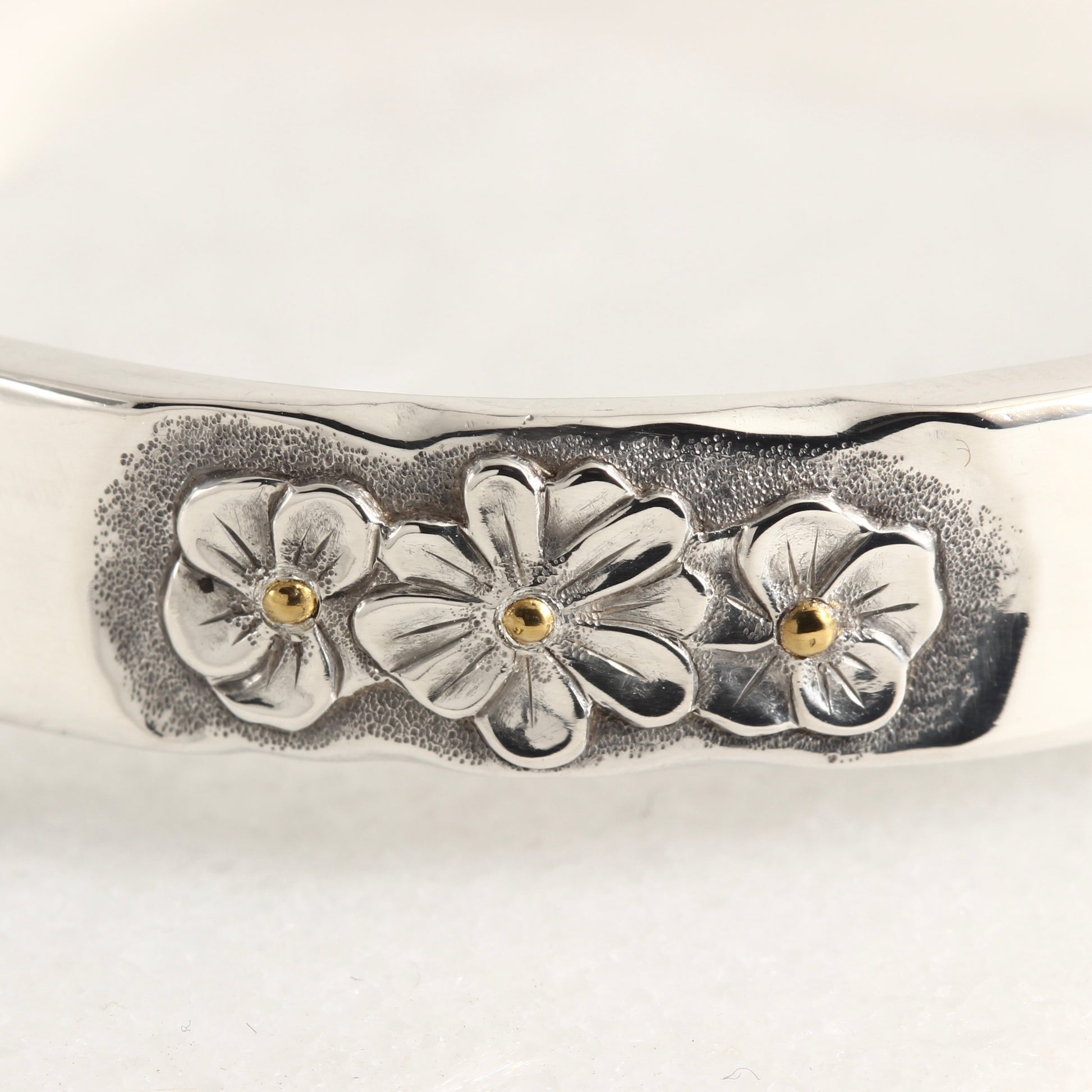 Close up of hand-formed sterling silver cuff with 24k gold accents and engraved texture