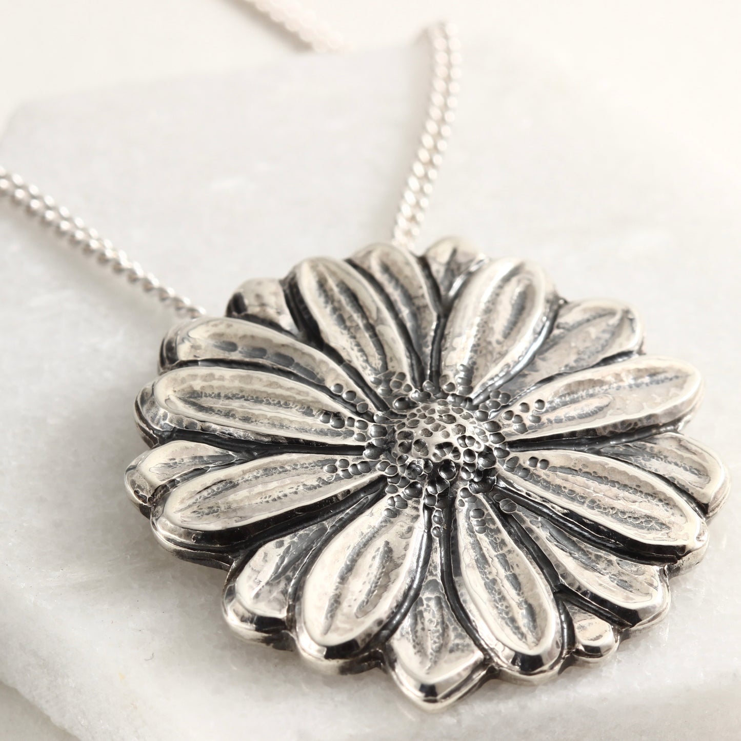 Wild Radiance Daisy Pendant in sterling silver, handcrafted flower necklace, on white marble 