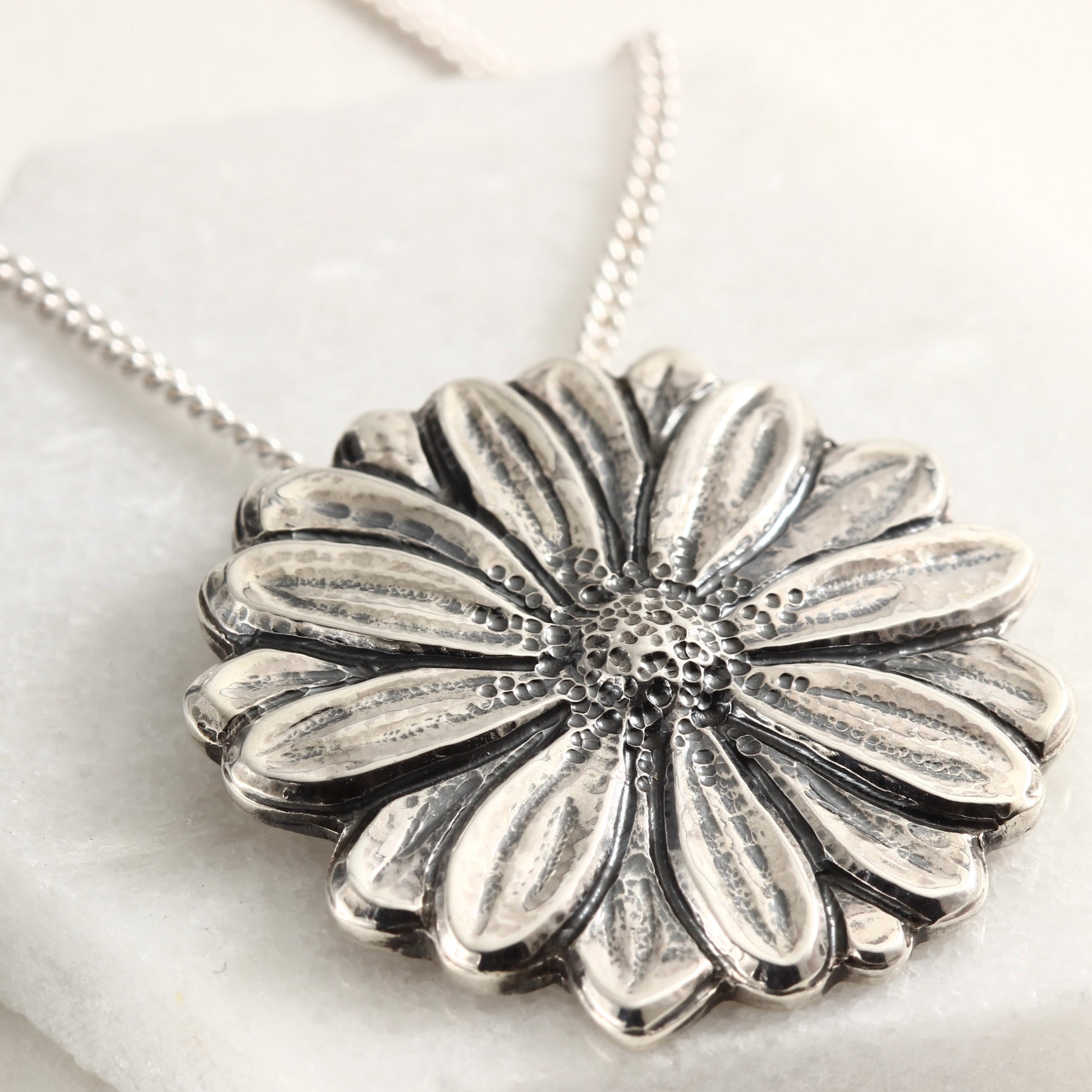 Wild Radiance Daisy Pendant in sterling silver, handcrafted flower necklace, on white marble 