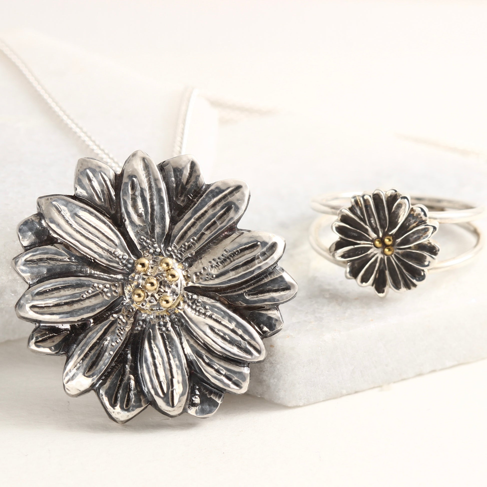 Wild Radiance Daisy Pendant and Ring with gold centers, shown on white marble background