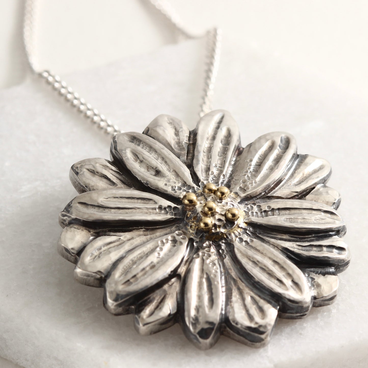 Wild Radiance Daisy Pendant with gold center in sterling silver on white marble background