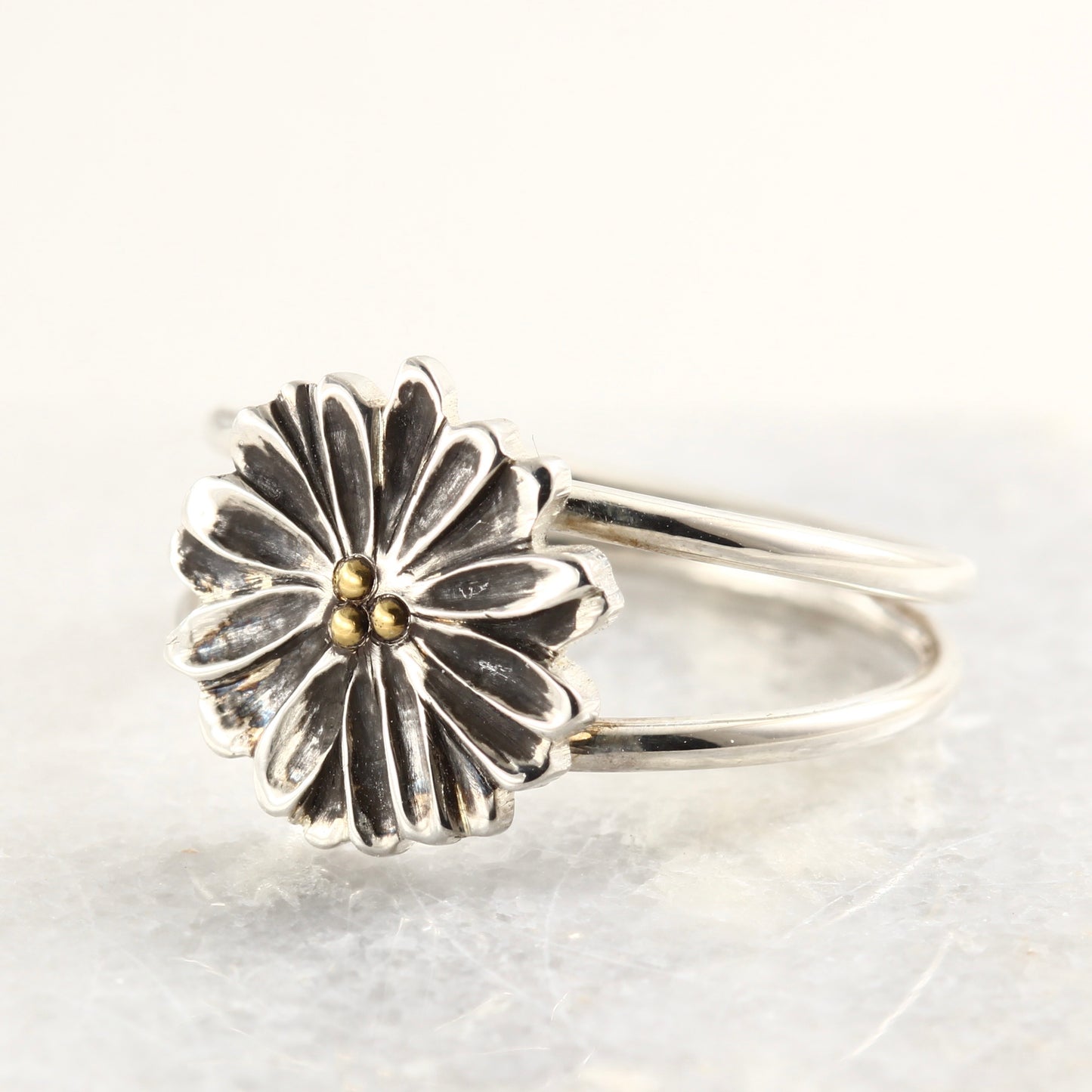 Wild Radiance Ring with gold center in sterling silver, a handcrafted flower ring, on a white marble tile